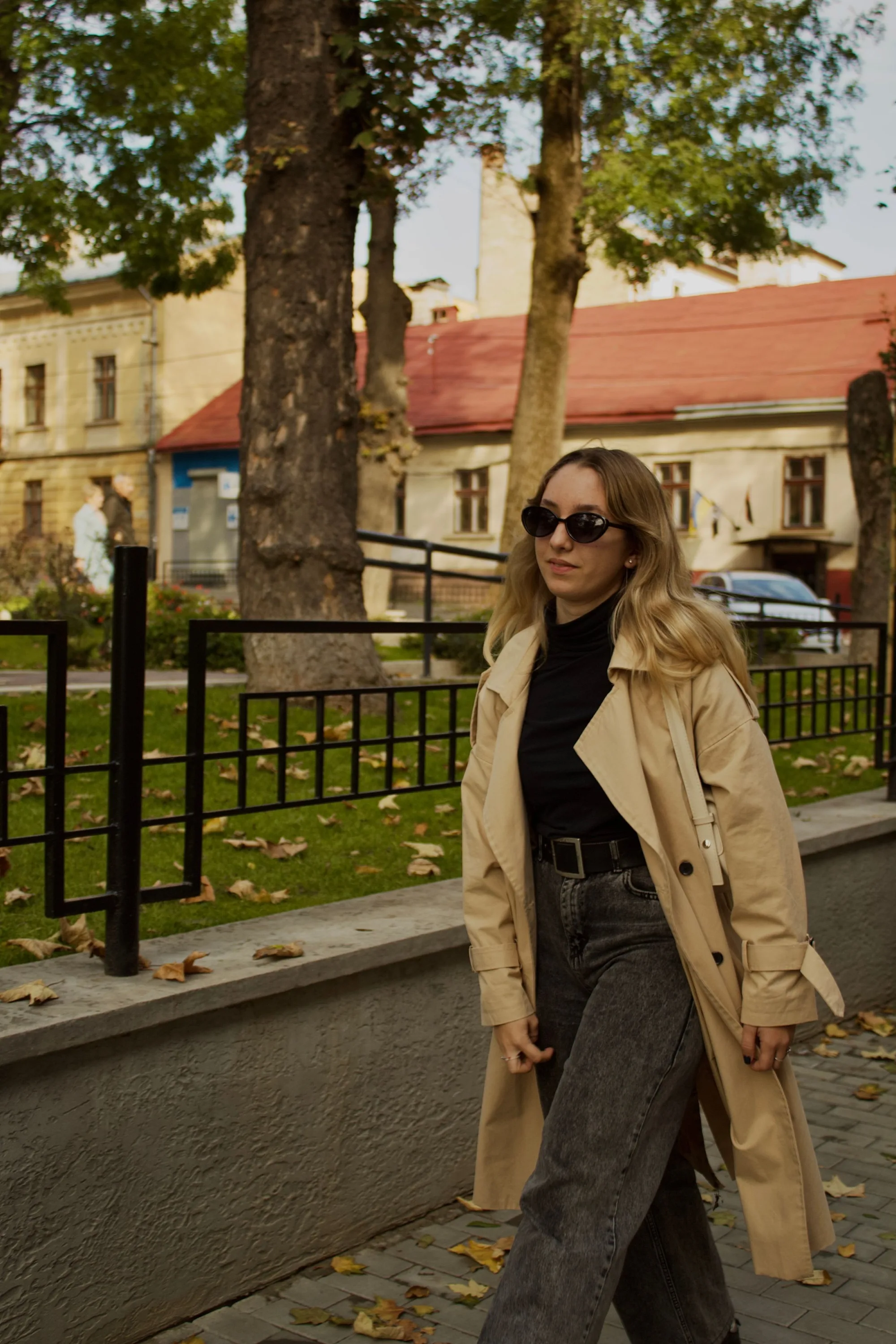 A woman in a trench coat walking under autumn trees